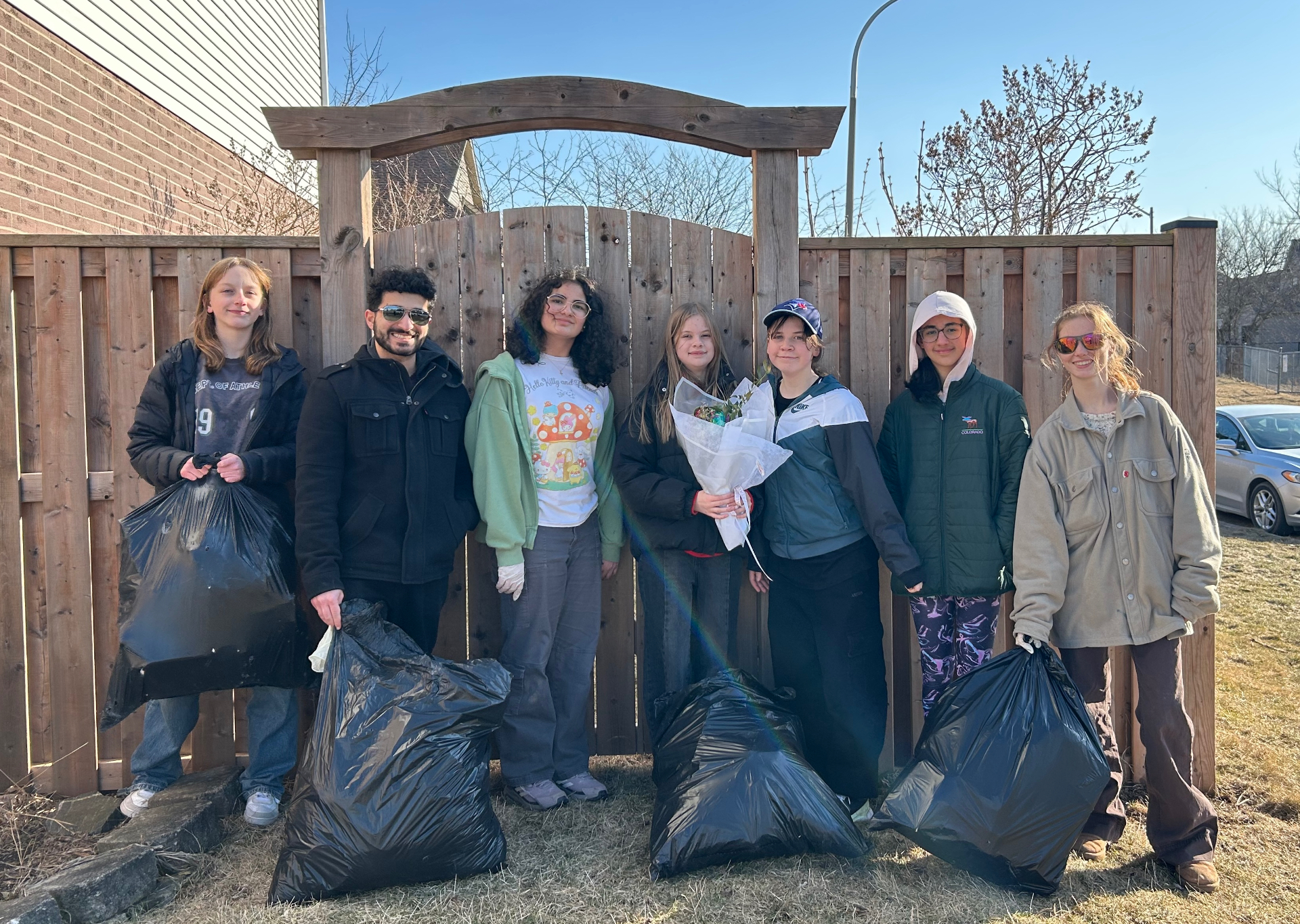 A group of junior youth and their animator outdoors after a neighbourhood clean-up, holding bags and smiling together.